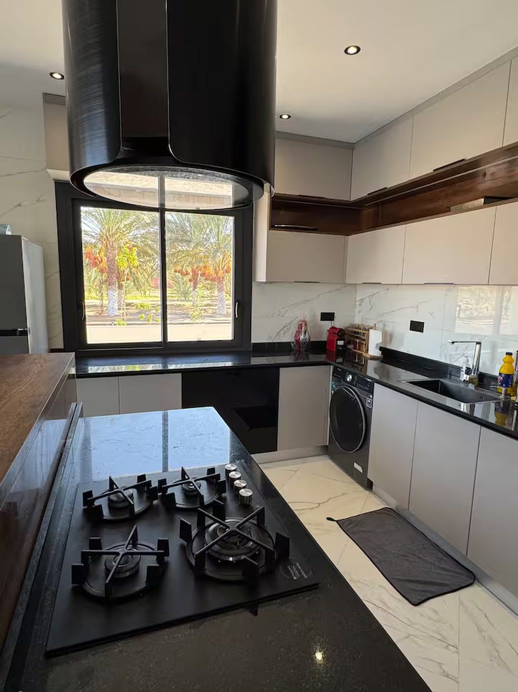 Una cocina moderna con estufa a gas, horno empotrado, lavadora y ventana con vista a árboles.