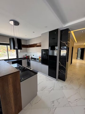 A modern kitchen with a central island, built-in appliances, and a large window providing natural light. - Villa in the heart of a palm grove (Mekhadma)