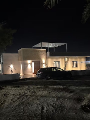 Un edificio moderno con un coche estacionado al frente, un espacio exterior cubierto y una entrada bien iluminada.