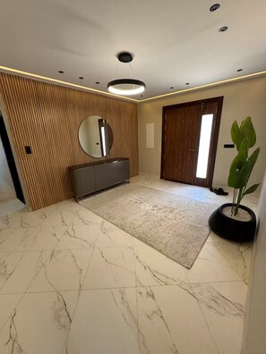 A hallway with a marble floor, a wooden panel wall, a round mirror, a grey cabinet, a potted plant, and a door. - Villa in the heart of a palm grove (Mekhadma)