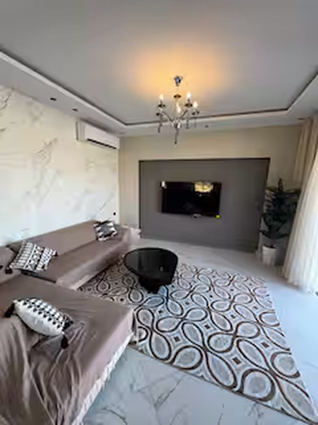 Un dormitorio moderno con una cama grande, un televisor instalado en la pared y una lámpara de techo.