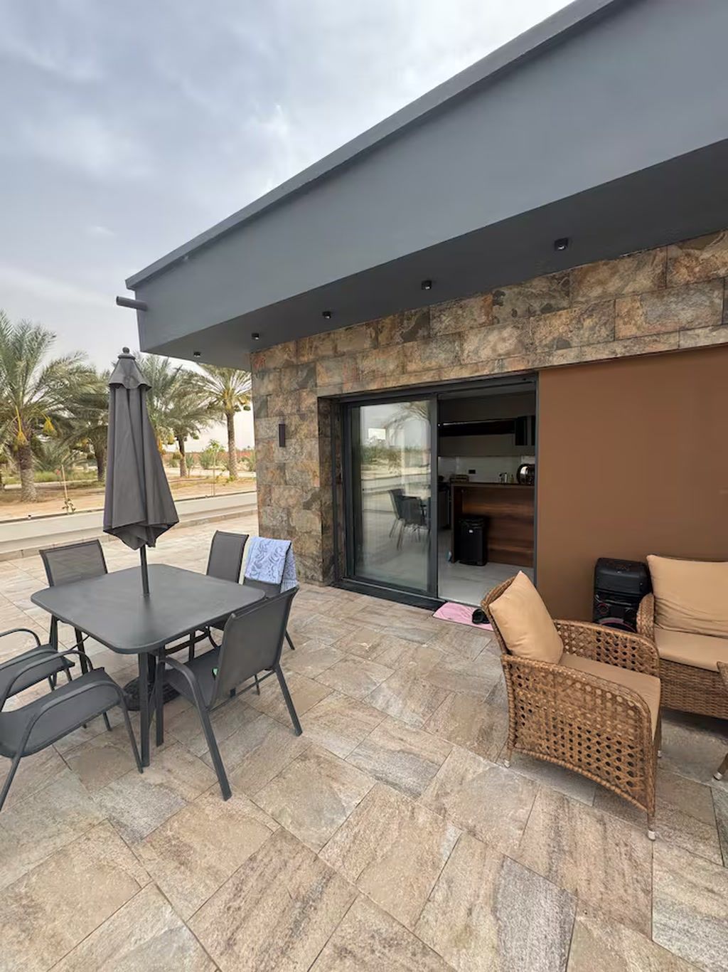 Un patio al aire libre con una mesa y sillas, un sofá de mimbre y una puerta de cristal que da a un espacio interior.