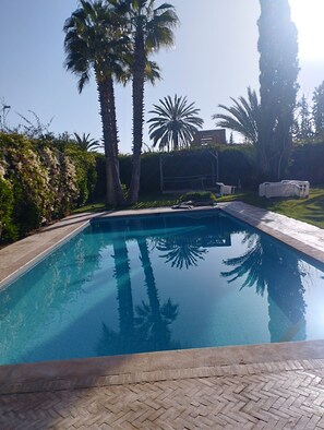 A rectangular swimming pool with clear blue water, surrounded by a brick deck, palm trees, and a hedge. - STUNNING VILLA - 4 BEDROOMS - PRIVATE POOL - QUIET LOCATION (Unknown)