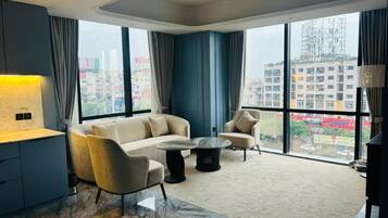 A modern hotel room with a large window, a sofa, a chair, a small round table, and a lamp.