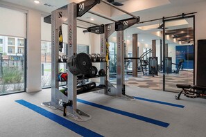 Un gimnasio con equipo de levantamiento de pesas, alfombra azul y ventanas amplias.