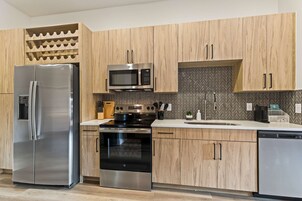 A modern kitchen with stainless steel appliances, wooden cabinetry, and a herringbone tile backsplash.