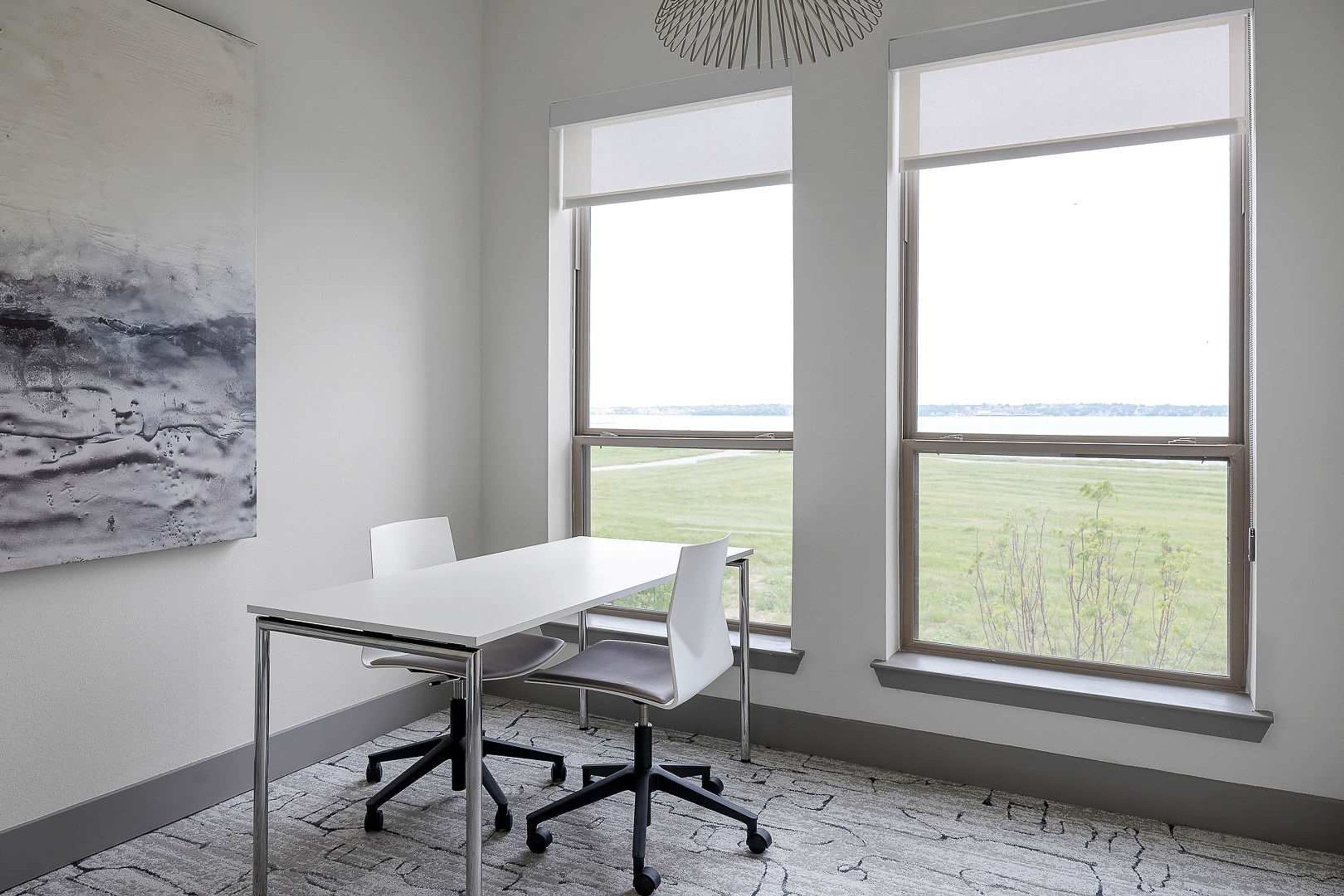 A conference room with a large table, two chairs, and two windows with a view of a field.