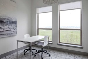 A conference room with a large table, two chairs, and two windows with a view of a field.