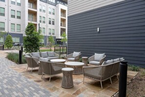 Eine Terrasse im Freien mit Korbmöbeln, einem kleinen Baum und einem Gebäude im Hintergrund.