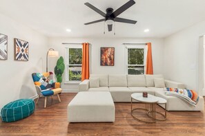 A modern living room with a sectional sofa, a coffee table, a colorful armchair, and a ceiling fan. - Movie Theatre Southpark Patio WFH Setup (Charlotte)