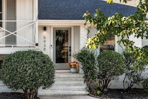 A white house with a dark roof, a number '5938' on the door, and a small porch with steps and a potted plant. - Movie Theatre Southpark Patio WFH Setup (Charlotte)