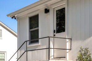 A white building with a door, two windows, and a small porch with a metal railing. - Movie Theatre Southpark Patio WFH Setup (Charlotte)
