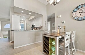 A modern kitchen with white cabinets, a central island, and a dining area with a wooden table and white chairs. - Just Listed! Welcome to The Cypress House at La Cita -Golf Course Views and Pool (Titusville)