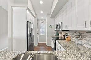 A kitchen with white cabinets, stainless steel appliances, a granite countertop, and a clock on the wall. - Just Listed! Welcome to The Cypress House at La Cita -Golf Course Views and Pool (Titusville)