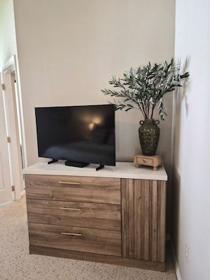 A flat-screen TV on a wooden cabinet with drawers, a small vase with a plant, and a white wall. - Just Listed! Welcome to The Cypress House at La Cita -Golf Course Views and Pool (Titusville)