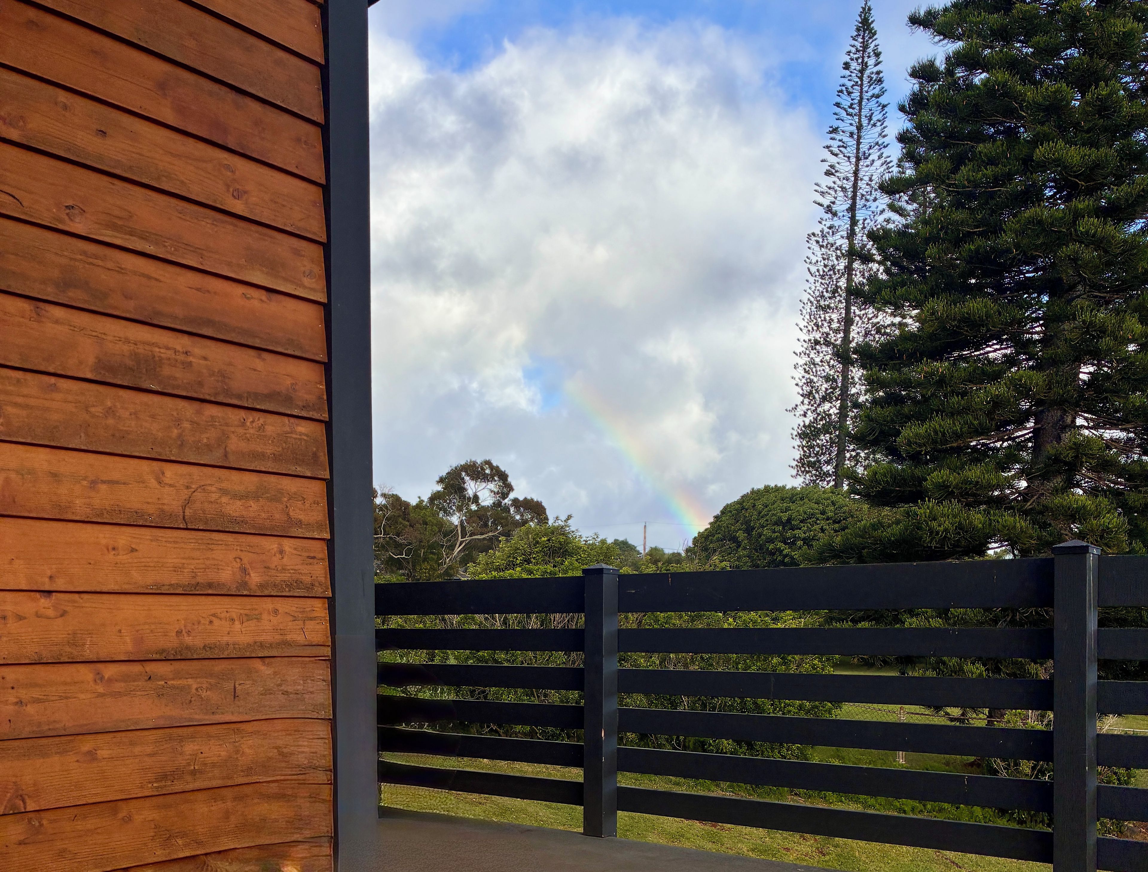 Une structure en bois offrant une vue sur un arc-en-ciel et une clôture.