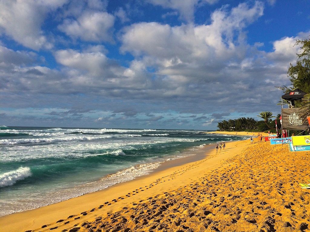A beach with footprints leading to the water, a lifeguard tower, and a clear sky.