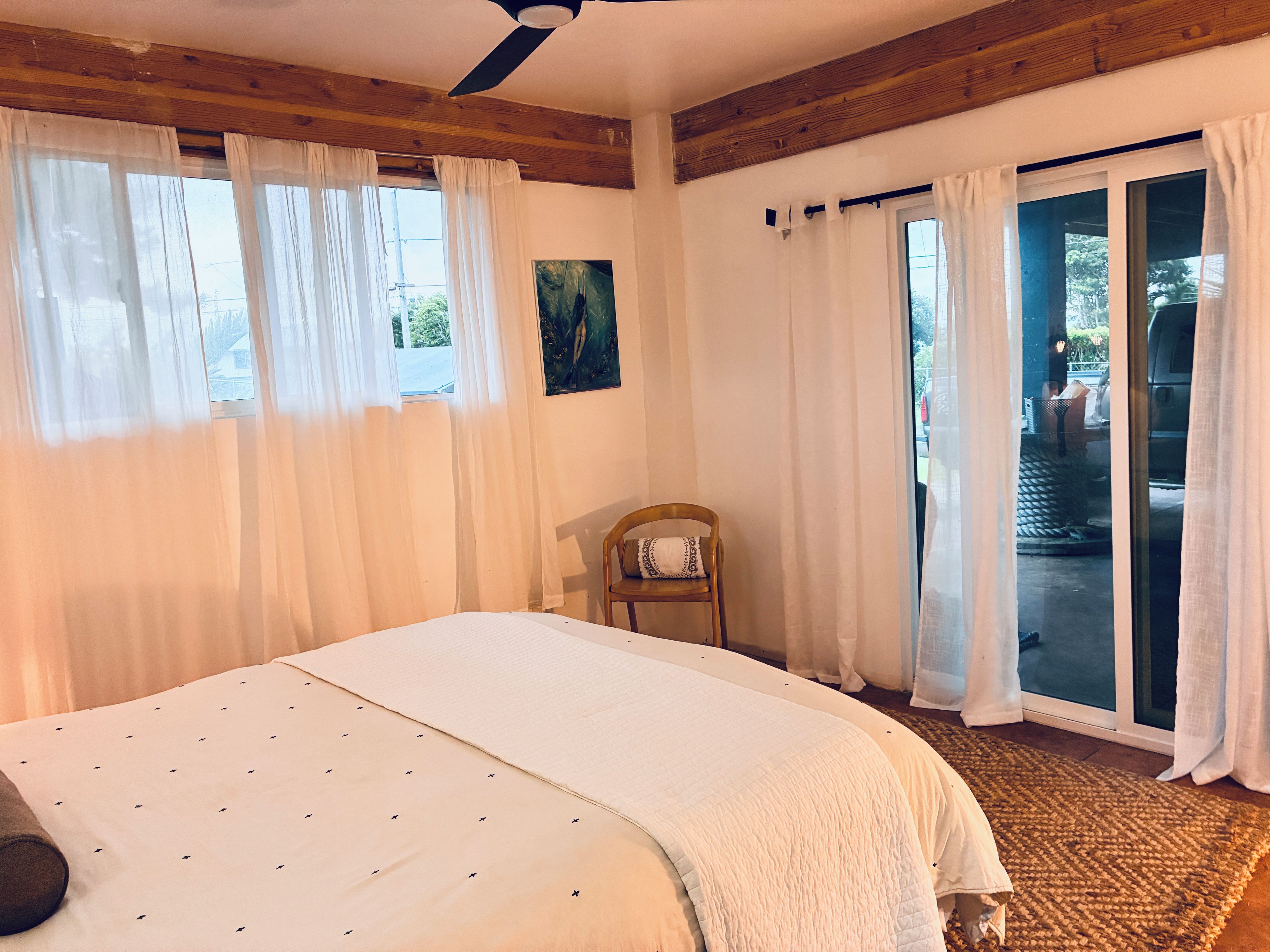Une chambre à coucher avec un lit, une chaise, un tableau et une vue à travers une porte vitrée.