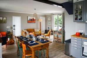 A dining area with a wooden table set for four, surrounded by chairs, and a kitchen area with cabinets and a stove. - Beach House in Deauville (Benerville-sur-Mer)