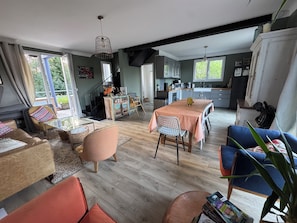 A spacious living area with a dining table, chairs, and a kitchen in the background. - Beach House in Deauville (Benerville-sur-Mer)