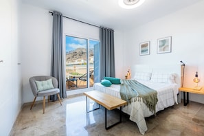 A modern bedroom with a bed, a chair, a bench, and a balcony with a view. - Playa Negra 1 - Two Bed Townhouse (Puerto Santiago)