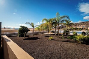 A landscaped outdoor area with a pool, palm trees, and a view of a hillside. - Playa Negra 1 - Two Bed Townhouse (Puerto Santiago)