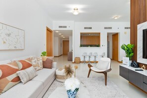 A modern living room with a sofa, armchairs, a coffee table, and a TV. There are plants and a painting on the walls. - Warm 2BR Marina View at Iris Blue (Dubai)