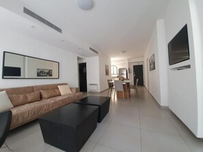 A modern living room with a sofa, coffee table, and a dining area in the background. - HaRav Kuk Royal Suites (Jerusalem)