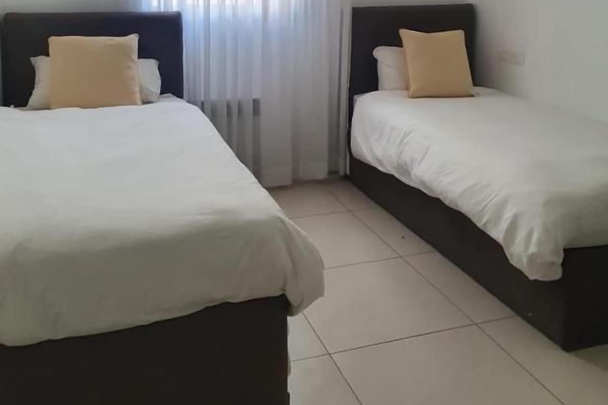 A hotel room with two beds, a large window with curtains, and a tiled floor.