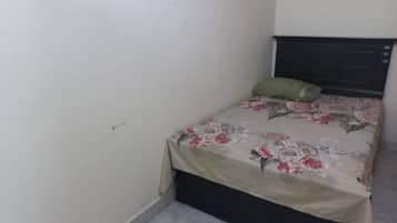 A small, single-bed room with a floral bedspread, a green pillow, and a dark headboard.