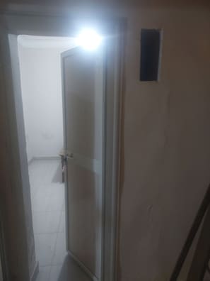 Una habitación con una puerta que da a otro espacio, suelo de baldosas y un pequeño enchufe en la pared.