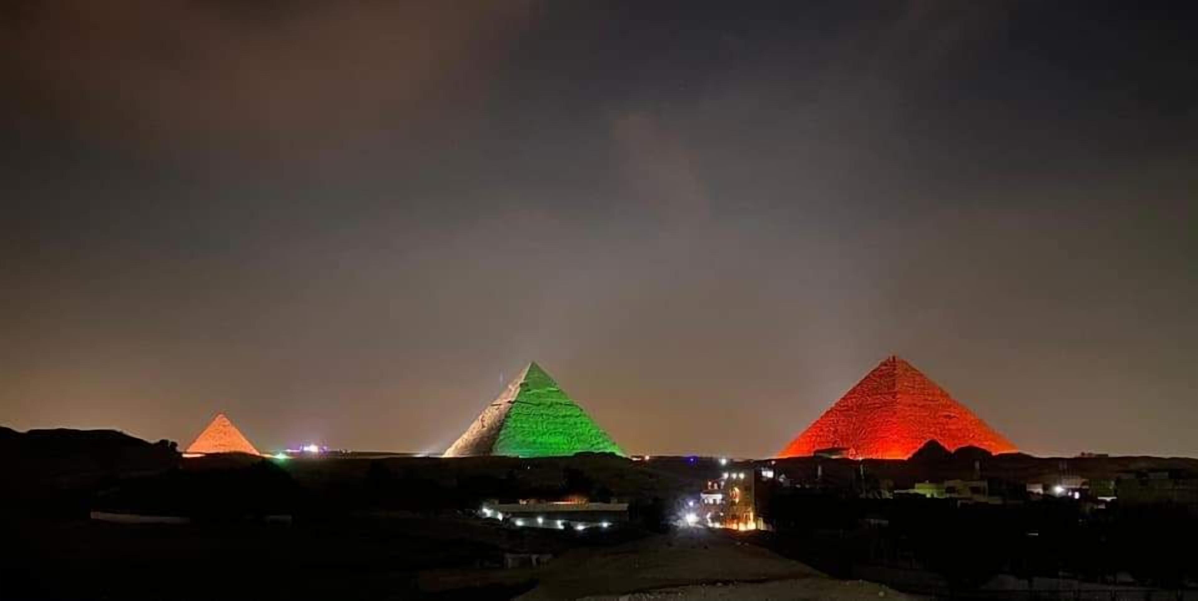 Trois pyramides illuminées la nuit par des jeux de lumière.