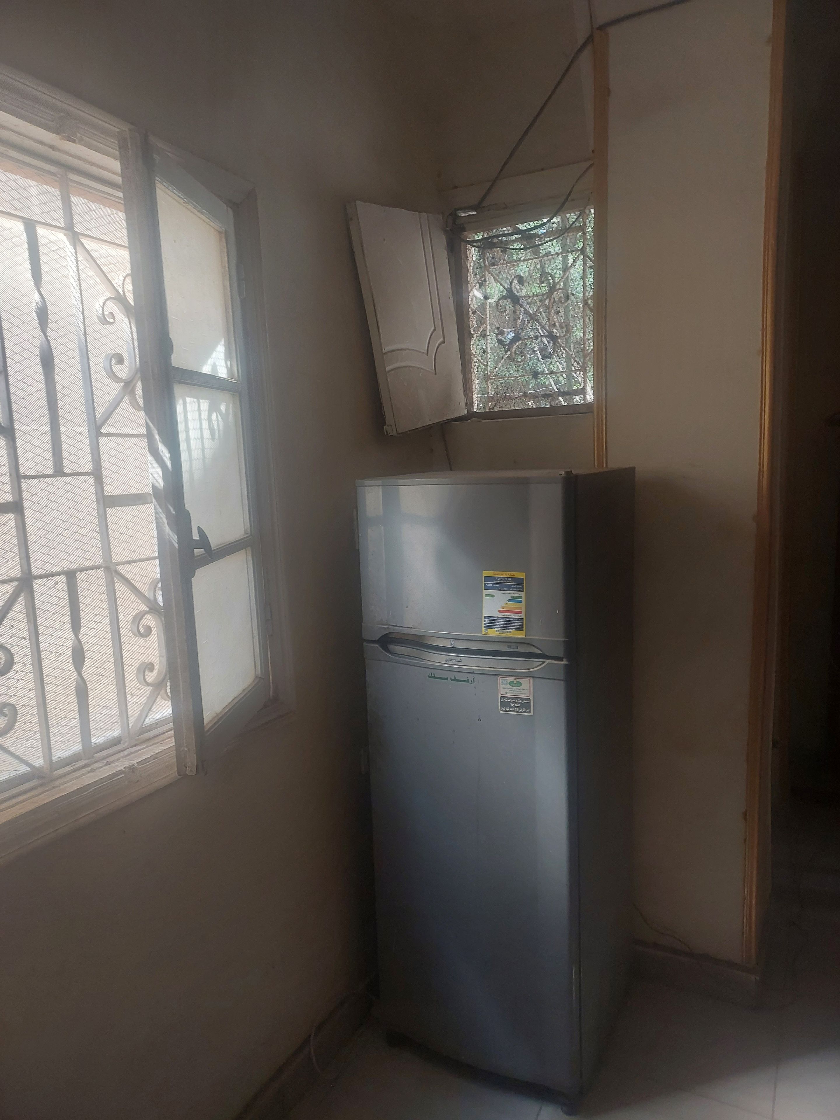 Une cuisine compacte équipée d’un réfrigérateur, d’une fenêtre avec une grille en métal et d’une petite fenêtre donnant sur les arbres.