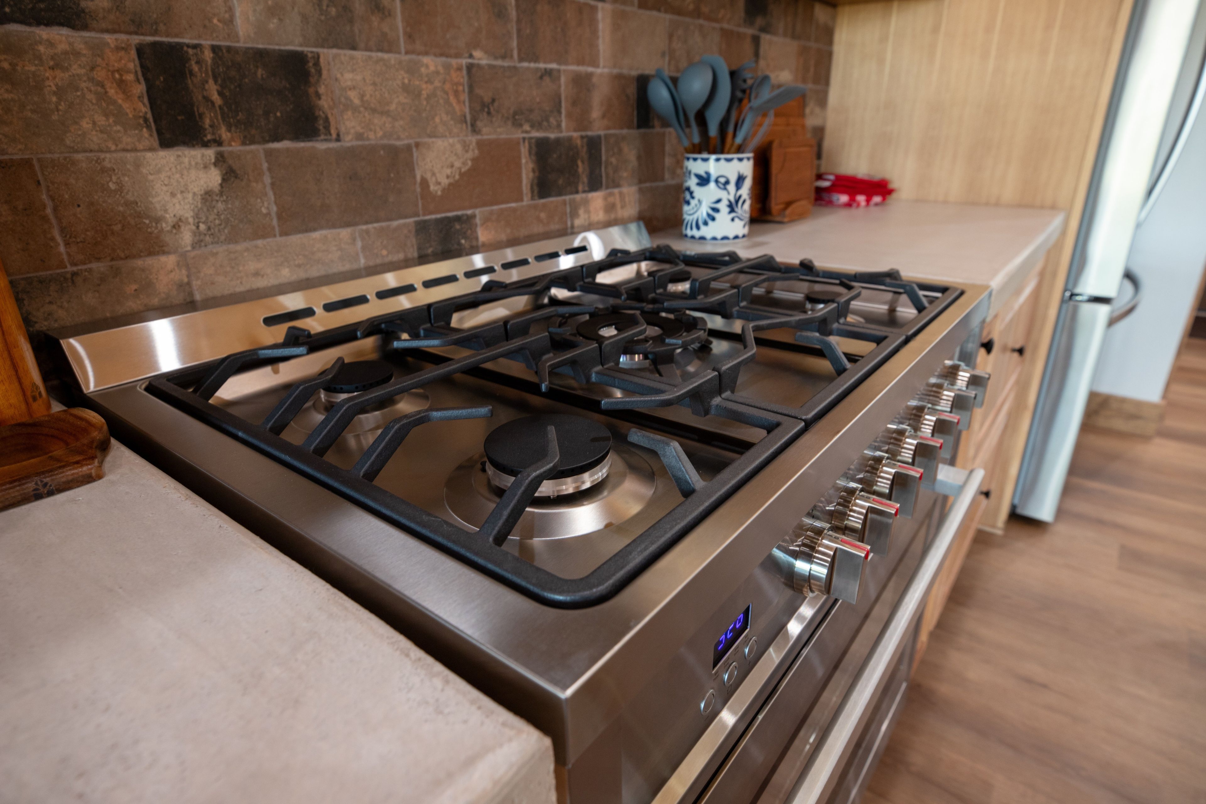 A stainless steel stove with four burners and a digital display, set against a kitchen backsplash with a stone pattern.
