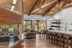 Amplia sala de estar con techo de madera, un ventanal grande y una zona de comedor con taburetes de bar.
