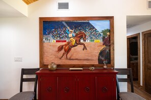 A painting of a rodeo scene on a wall above a red cabinet with drawers. - Guadalupe Bluff Trail House 5 Bedroom Home (Kerrville)