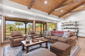 A spacious living area with a high ceiling, large windows, and a view of the outdoors. - Guadalupe Bluff Trail House 5 Bedroom Home (Kerrville)