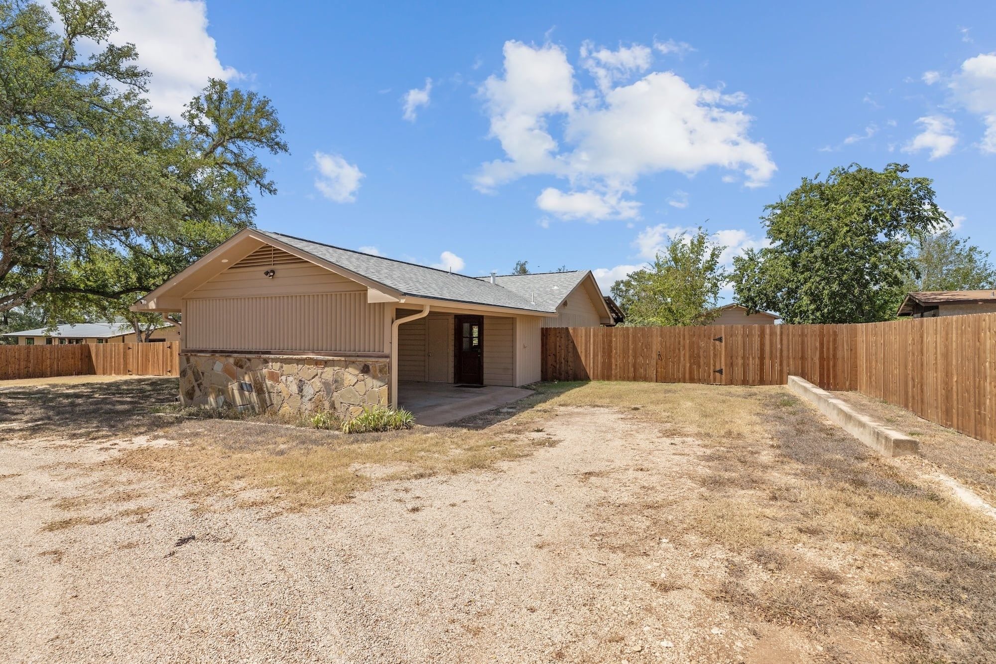 A single-story house with a garage, a stone foundation, and a wooden fence.