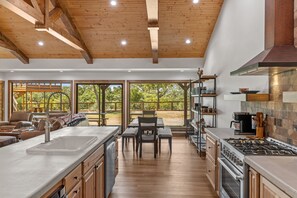 A modern kitchen with a large island, wooden cabinetry, and a view of the outdoors. - Guadalupe Bluff Trail House 5 Bedroom Home (Kerrville)
