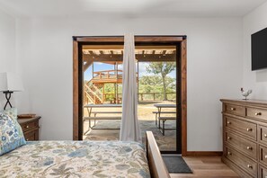 Une chambre à coucher comprenant un lit, une commode, une table de chevet et une fenêtre donnant sur une terrasse extérieure.