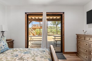 Un dormitorio con cama, cómoda, mesita de noche y ventana con vista a una terraza exterior.