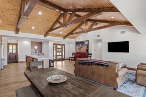 Un vaste espace de vie doté d’un haut plafond en bois, d’une table à manger, d’un canapé et d’un téléviseur fixé au mur.
