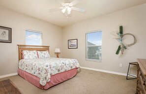 A bedroom with a bed, a ceiling fan, two windows, a wall-mounted decoration, and a dresser. - Shore Enough 3 Bedroom Home (Port Bolivar)