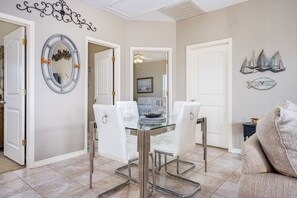 A dining area with a glass table and white upholstered chairs, a decorative mirror, and a wall with a nautical theme. - Shore Enough 3 Bedroom Home (Port Bolivar)