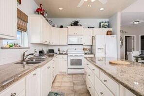 A kitchen with white cabinets, a microwave, a stove, and a refrigerator. - Shore Enough 3 Bedroom Home (Port Bolivar)
