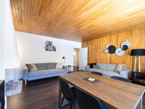 A modern living room with a wooden ceiling, two sofas, a dining table with chairs, and decorative wall art. - Bright central apartment - 4 guests (Val-d'Isère)