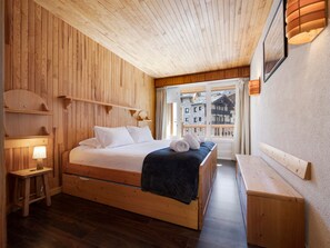 A wooden room with a bed, bedside table, and a window with a view of buildings. - Bright central apartment - 4 guests (Val-d'Isère)