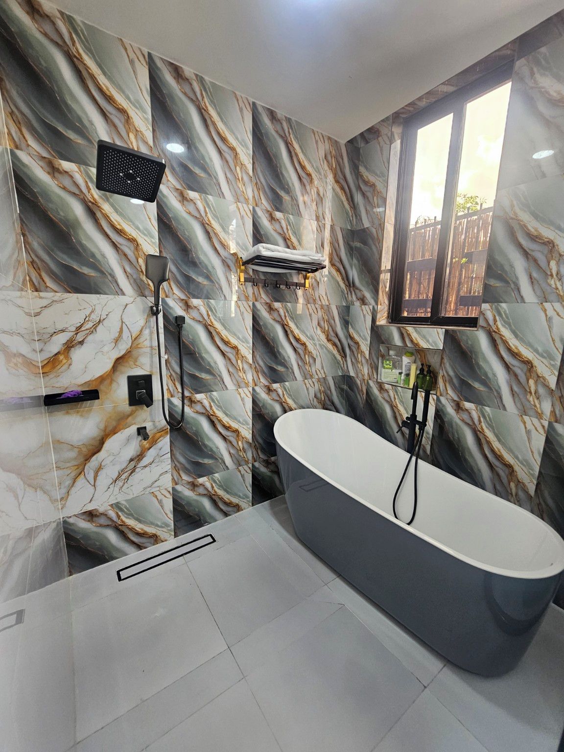 A modern bathroom with a freestanding bathtub, marble-patterned walls, and a window providing natural light.