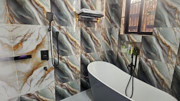 A modern bathroom with a freestanding bathtub, marble-patterned walls, and a window providing natural light.