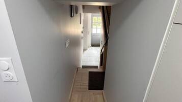 Een smalle gang met een houten vloer die leidt naar een kamer met een deur en een raam.